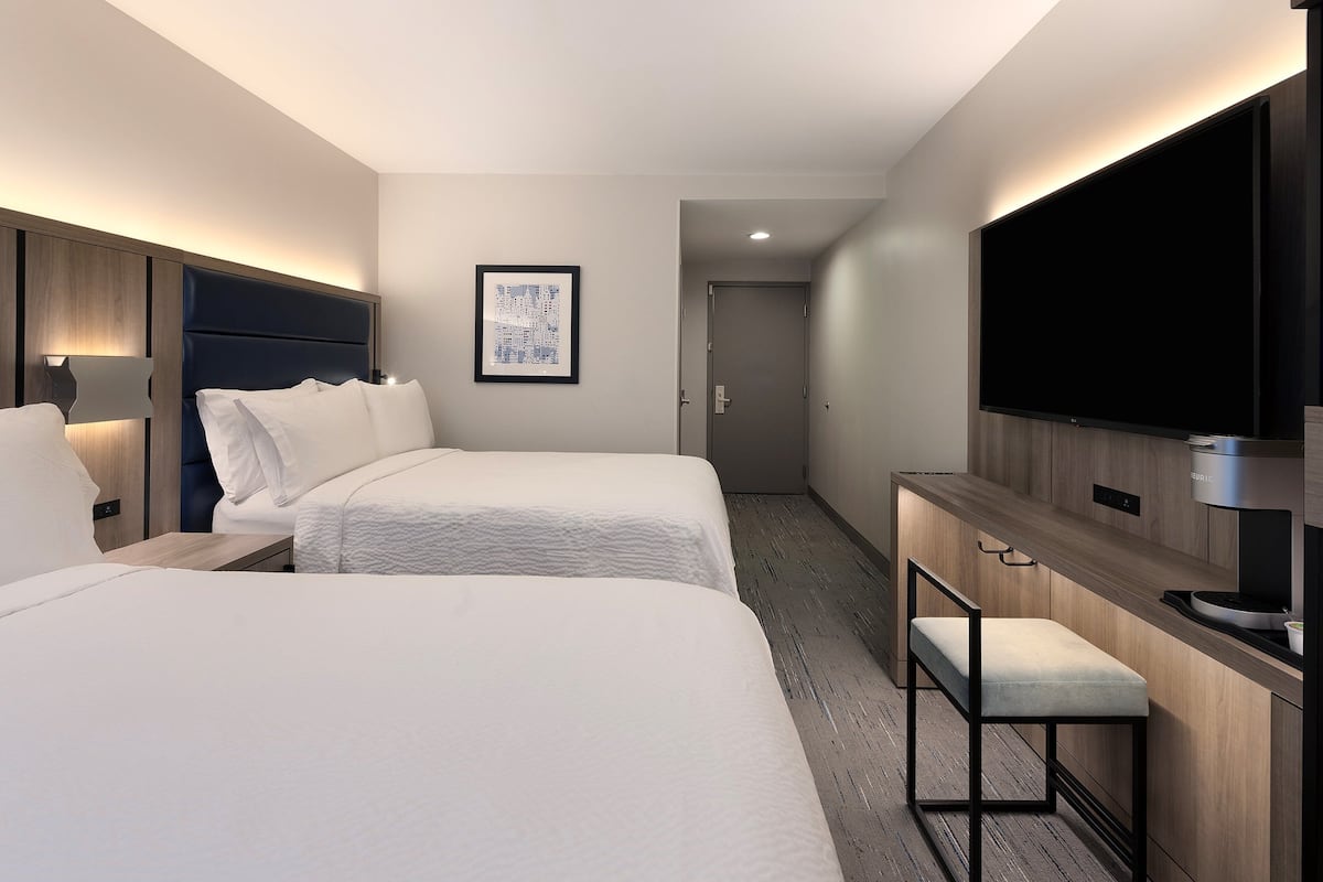 Habitació d'hotel amb dos llits, un escriptori, un televisor de pantalla plana i un quadre al mur.