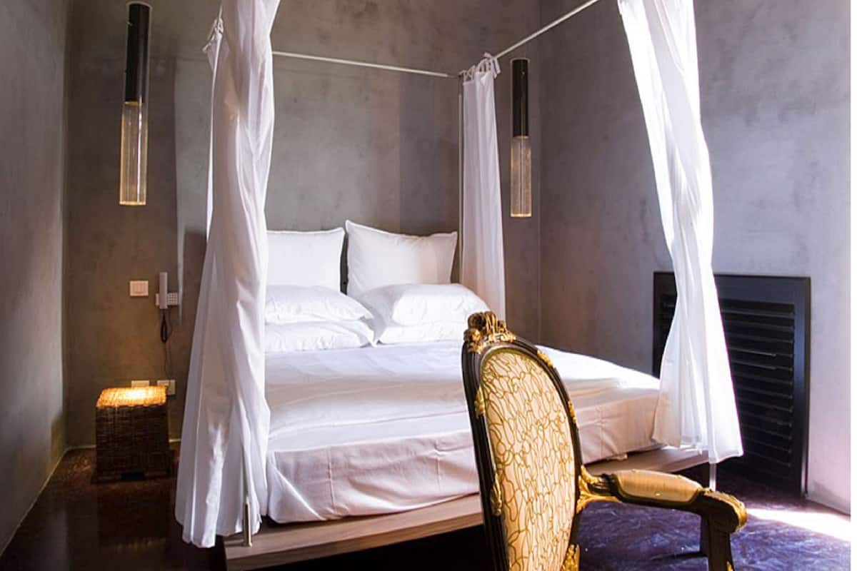 A bedroom with a four-poster bed, a chair, and a bedside table.