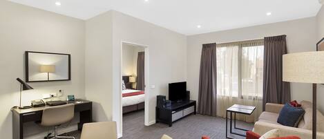 Habitación de hotel con cama, escritorio con computadora, televisor, mesa de comedor con sillas y sofá.