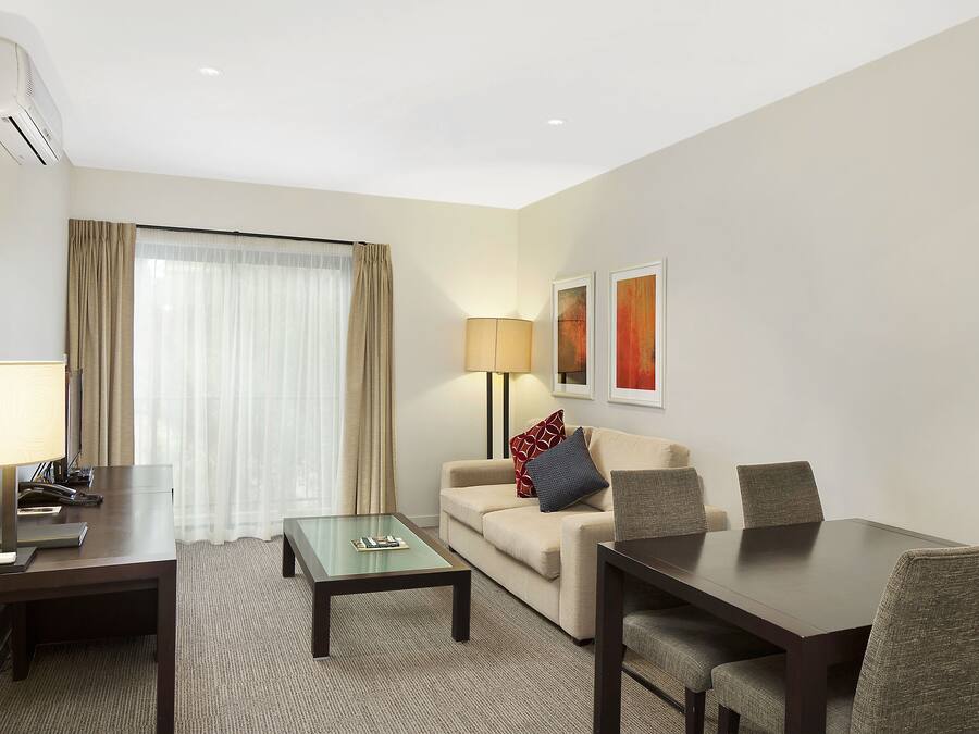 A hotel room with a sofa, a small table, a larger dining table, and a lamp.