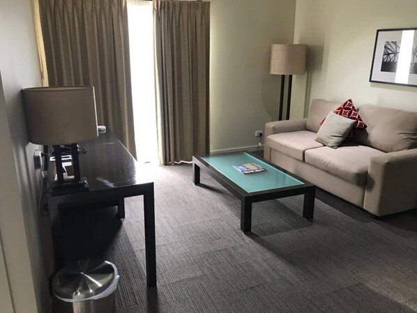 Una habitación de hotel con sofá, mesa de centro, lámpara y televisor.