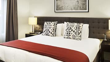 A hotel room with a large bed, a bedside table with a lamp, a framed picture on the wall, and an air conditioning unit.