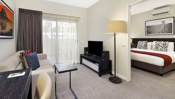 Una habitación de hotel con sofá, televisión, mesita de noche, lámpara y cama.