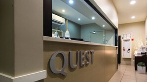 Una recepción con el nombre "QUEST" bien visible, un diseño interior moderno y una unidad de aire acondicionado.