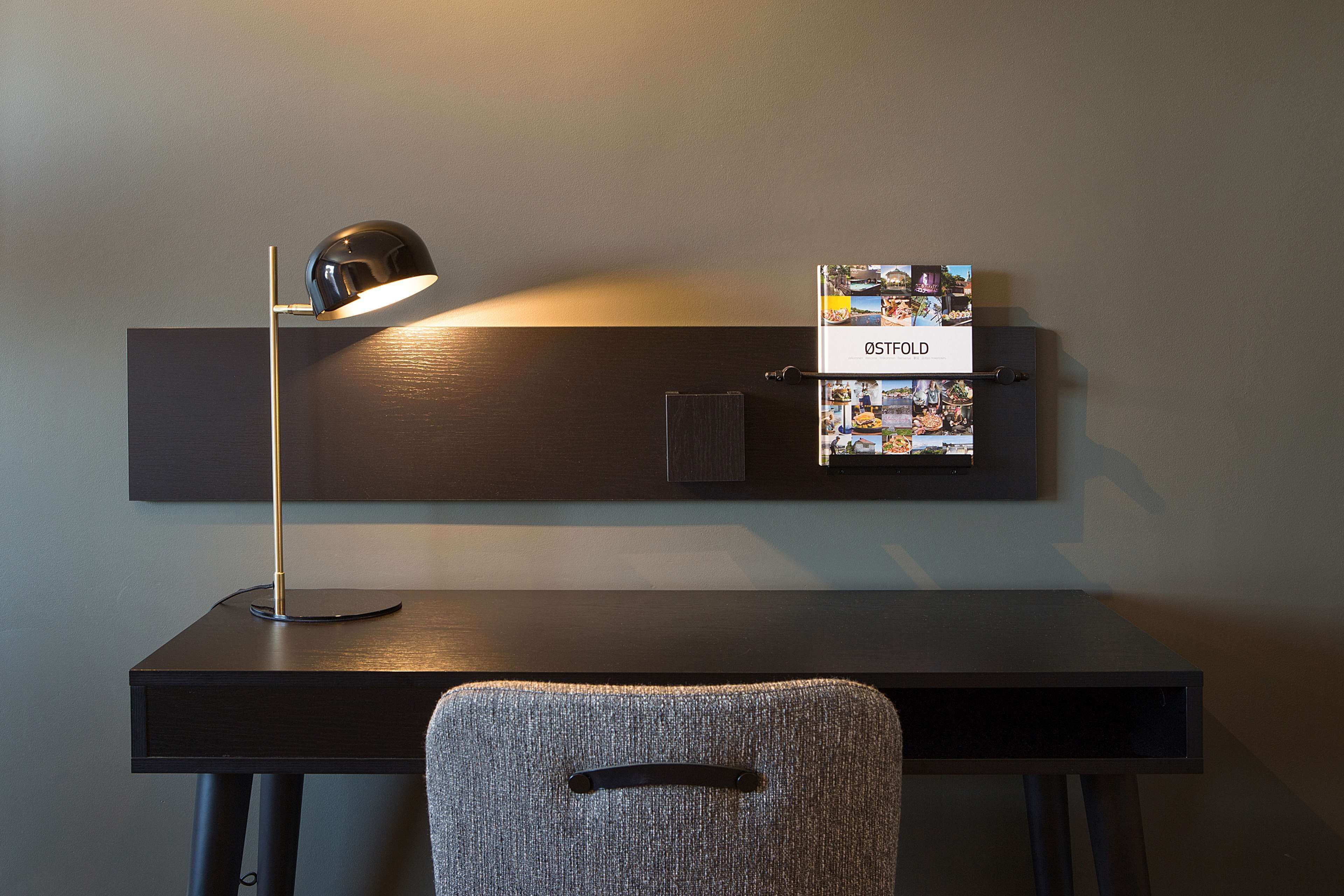 A modern workspace with a desk, a chair, a lamp, and a wall-mounted board displaying photos and the word "OSTROLD".