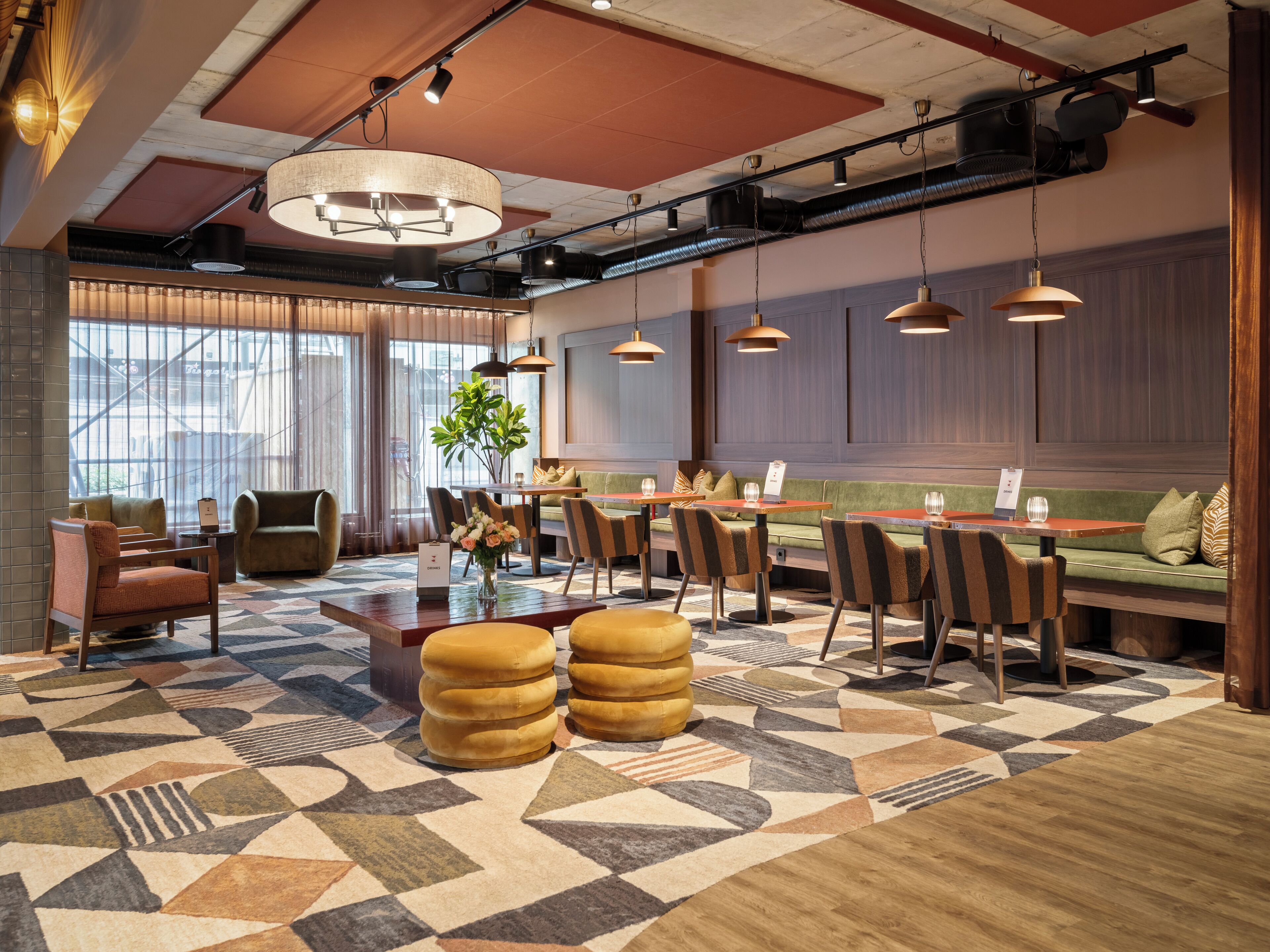 Un moderno vestíbulo de hotel con alfombra de estampado geométrico, diversas opciones de asientos que incluyen sofás y sillones, y un ventanal que ofrece vistas al exterior.