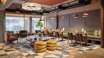 Un moderno vestíbulo de hotel con alfombra de estampado geométrico, diversas opciones de asientos que incluyen sofás y sillones, y un ventanal que ofrece vistas al exterior.