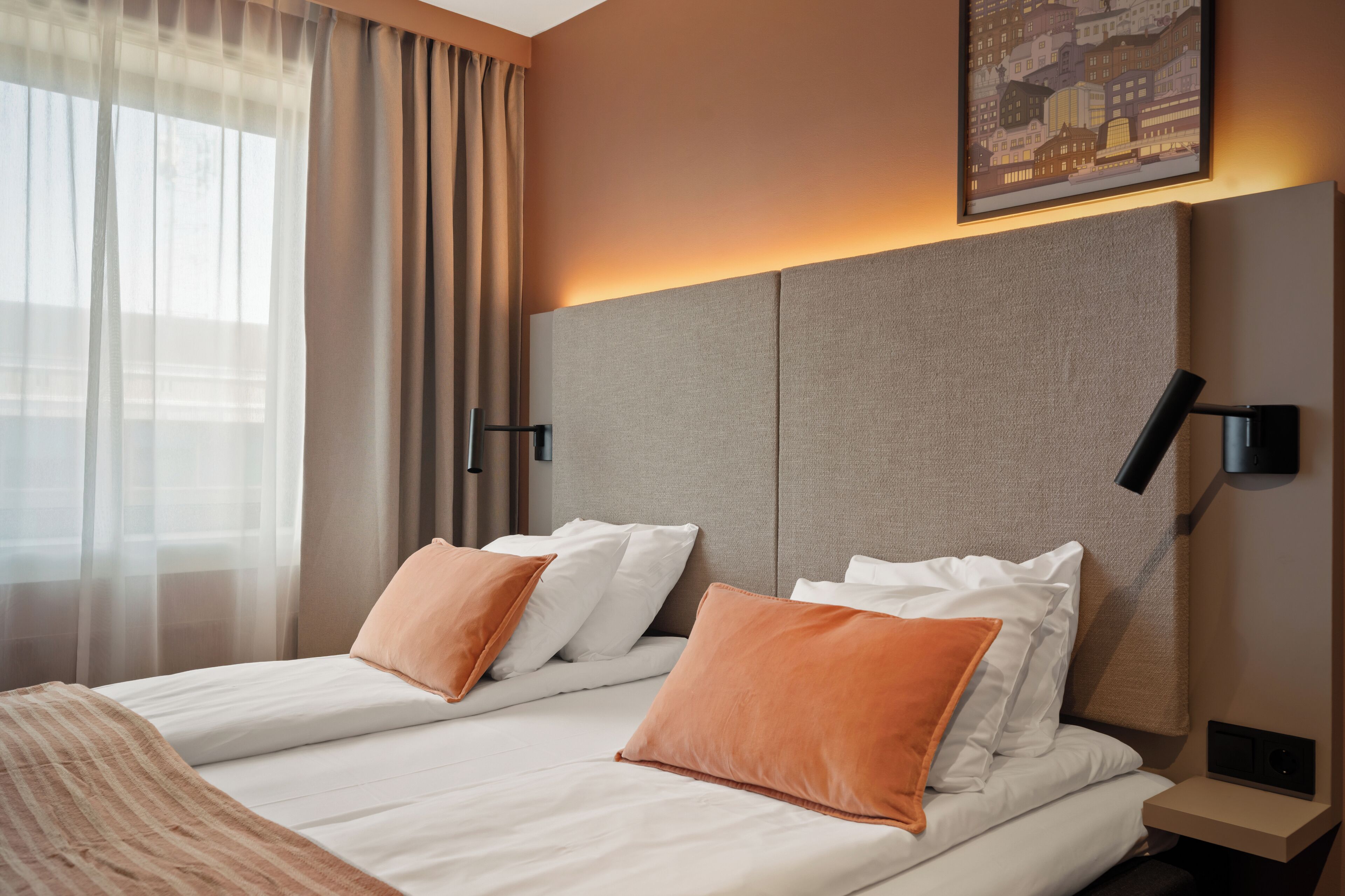 A hotel room with a large bed, two pillows, a bedside table, a lamp, and a painting on the wall.