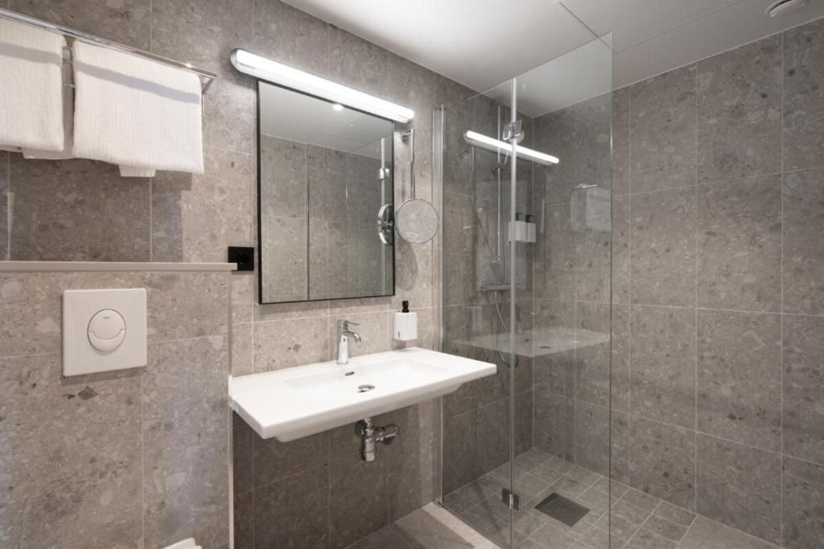 A modern bathroom with a glass-enclosed shower, a white sink, and a mirror above it.