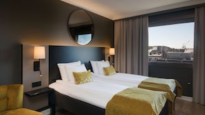 A hotel room with a large bed, two bedside tables, a round mirror, and a view of the city through the window.