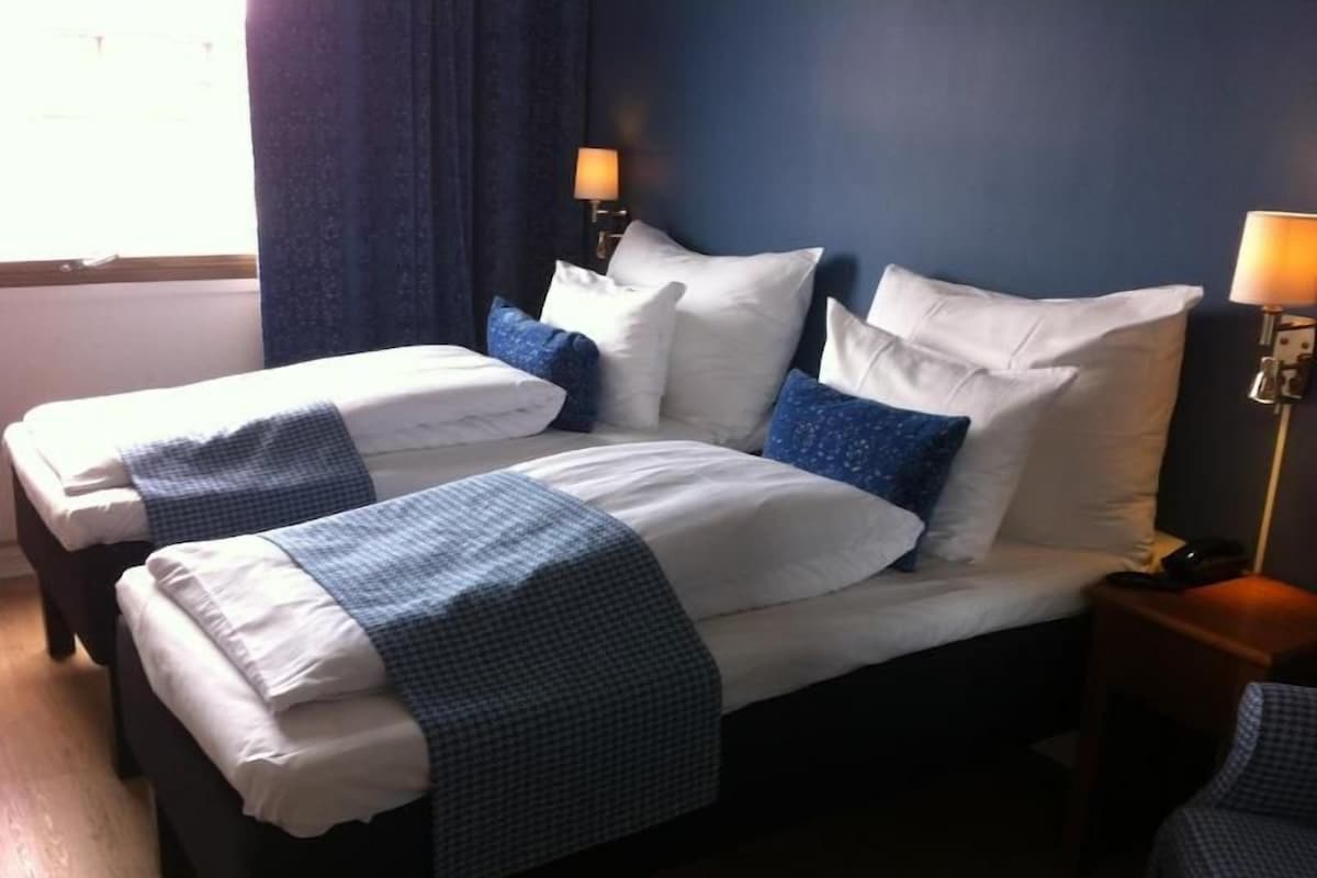 A hotel room with two beds, a nightstand, and a lamp.
