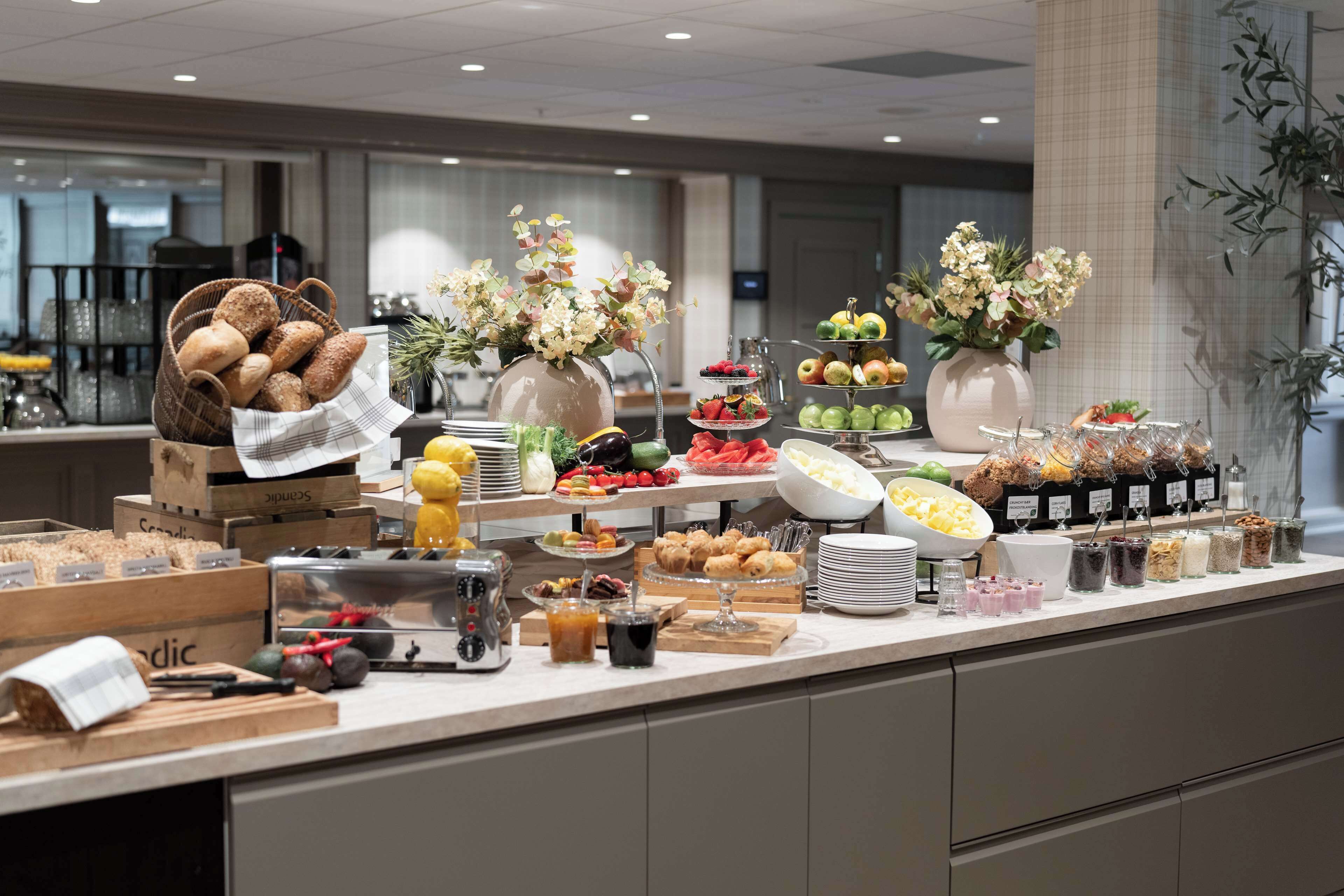 En buffet med et udvalg af mad og drikkevarer, herunder brød, frugt og desserter.