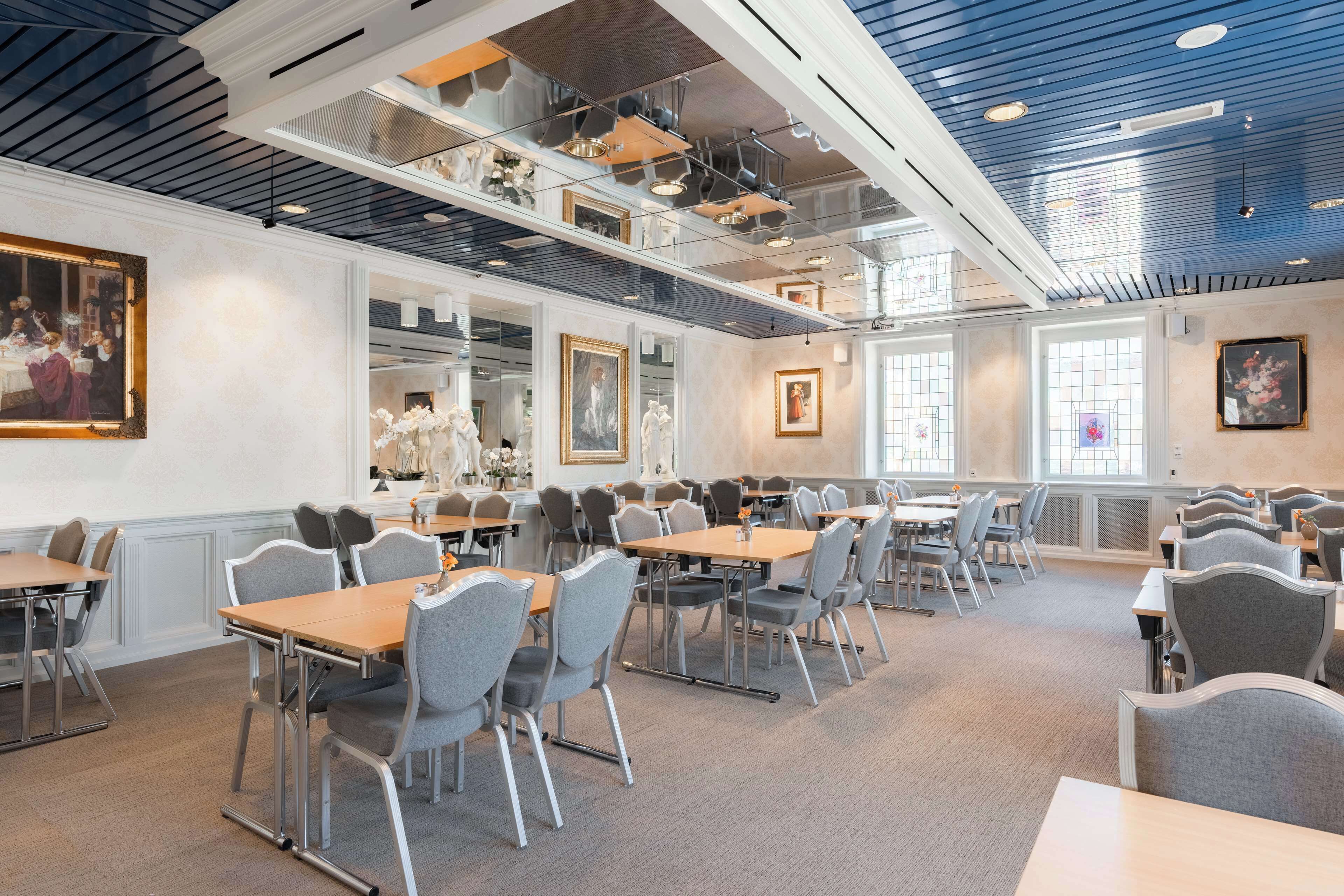 A spacious dining area with multiple tables and chairs, large windows, and ceiling lights.