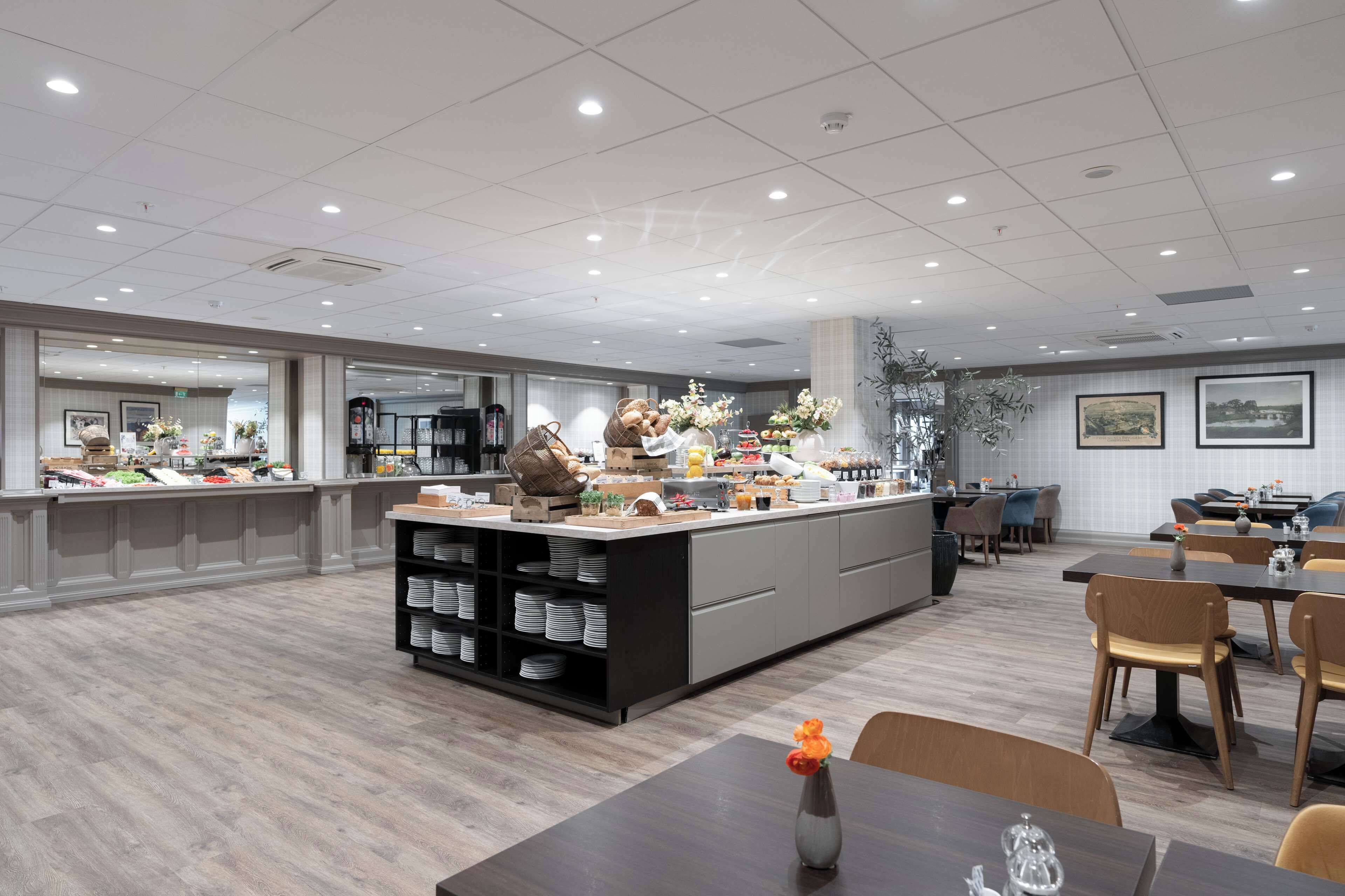 En moderne hotelspisestue med en central ø, siddepladser og et buffetbord.