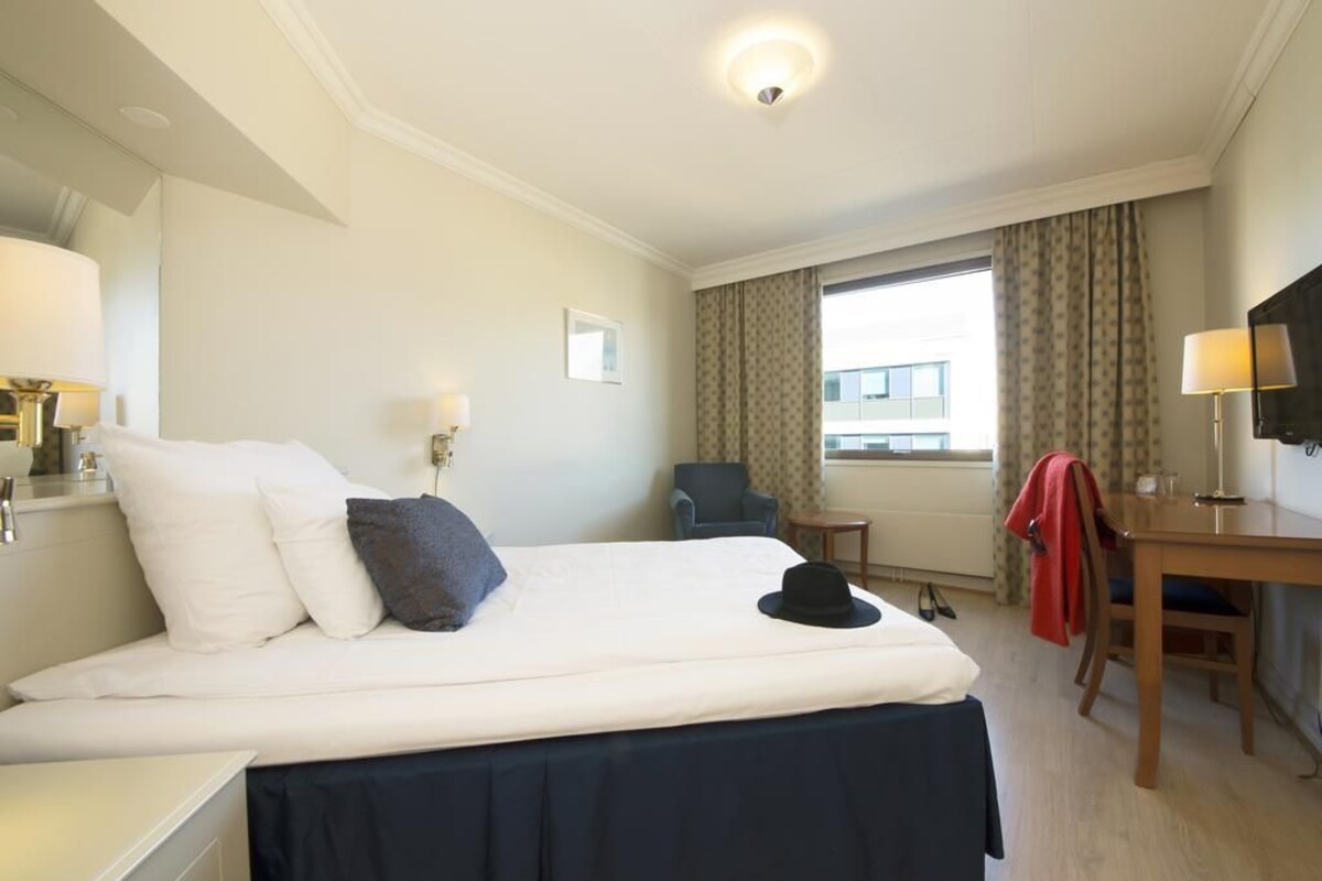 A hotel room with a bed, a desk, a chair, a television, and a window with curtains.