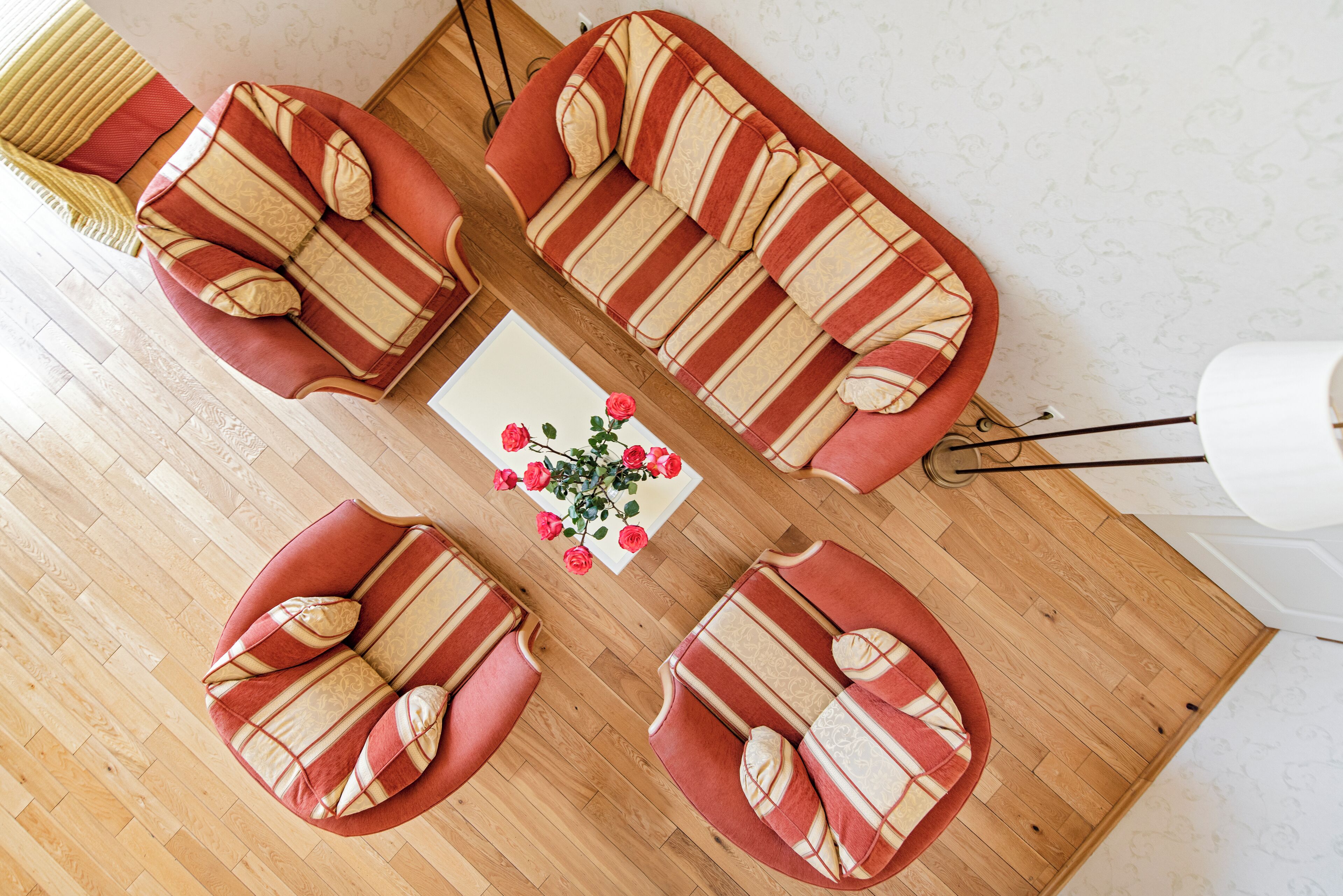 A top-down view of a room with a wooden floor, a striped sofa set, a small table with a vase of flowers, and a lamp.
