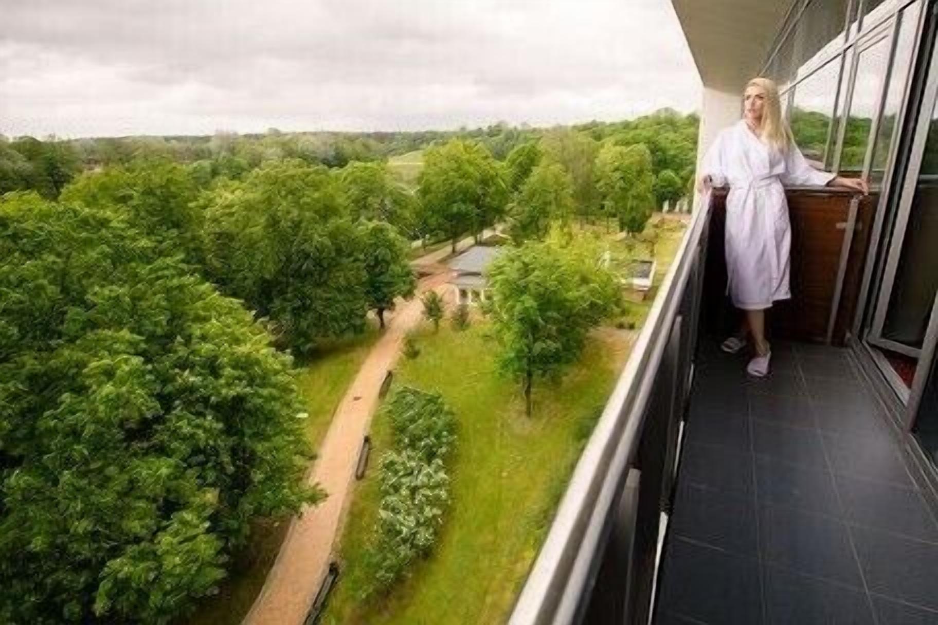 A balcony with a view of a green landscape and a building in the distance.