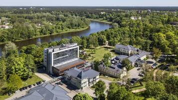 An aerial view of a hotel complex with a modern building, surrounded by lush greenery and a river.