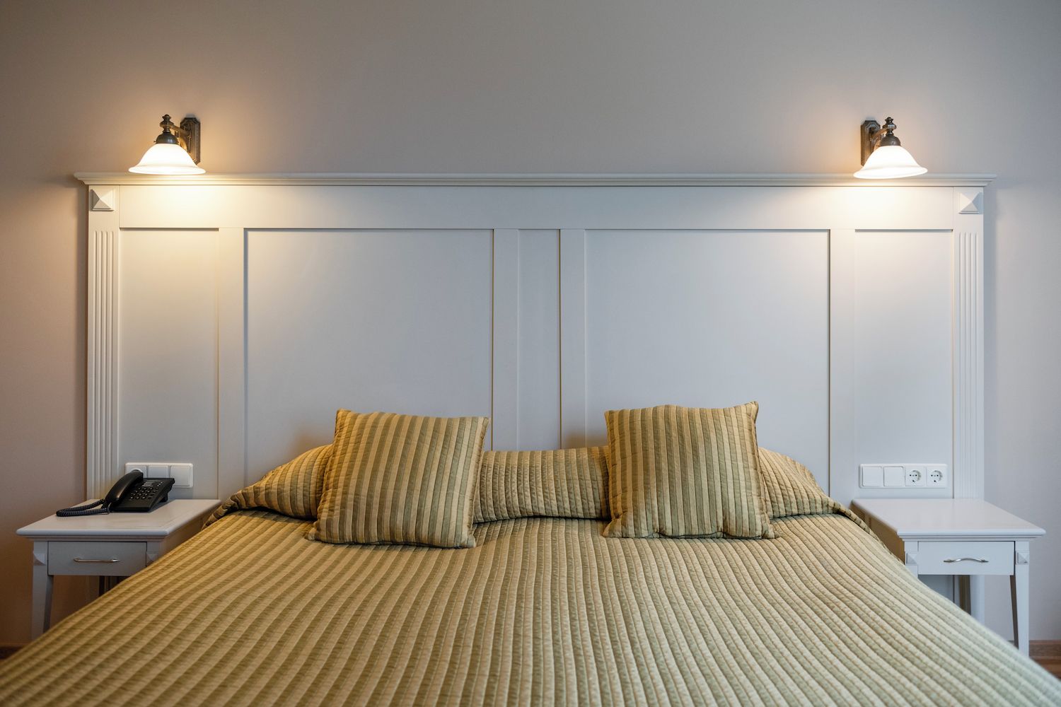 Quarto de hotel com uma cama, duas mesas de cabeceira, telefone e luminárias fixadas na parede.
