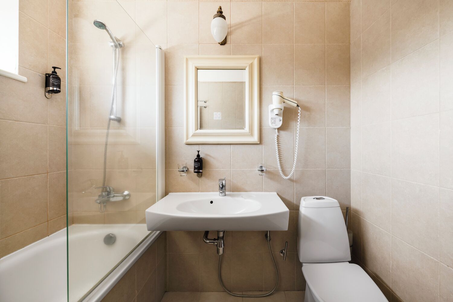 A bathroom with a glass-enclosed shower, a white sink, a toilet, and a mounted mirror.