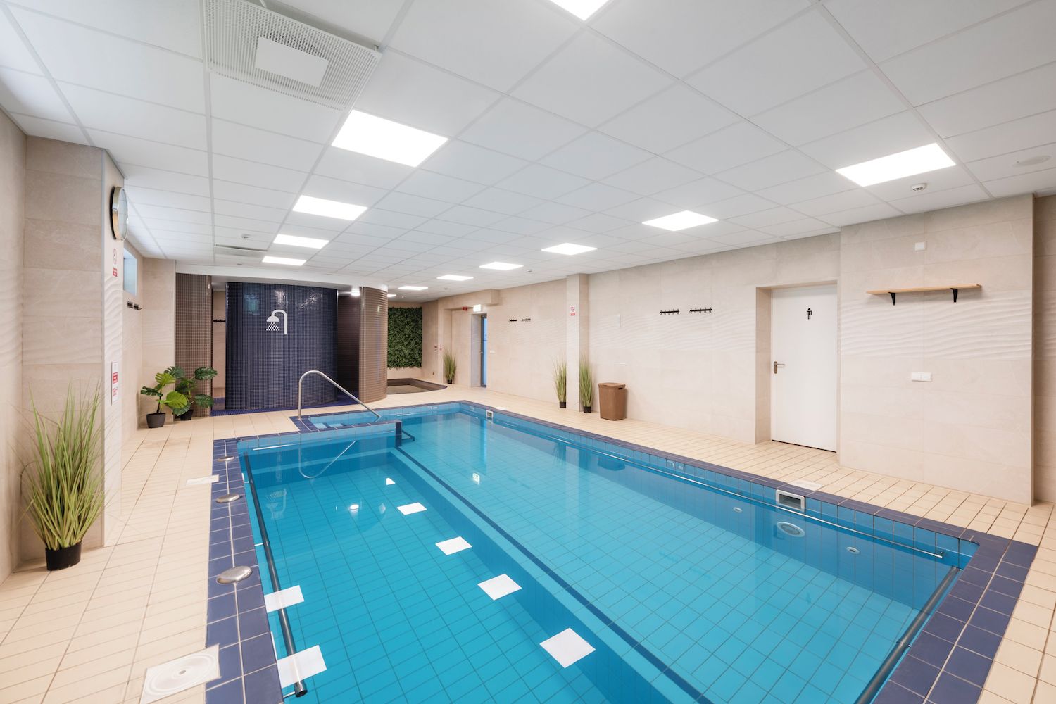 An indoor swimming pool with clear lanes, a changing room, and a door leading to a shower area.
