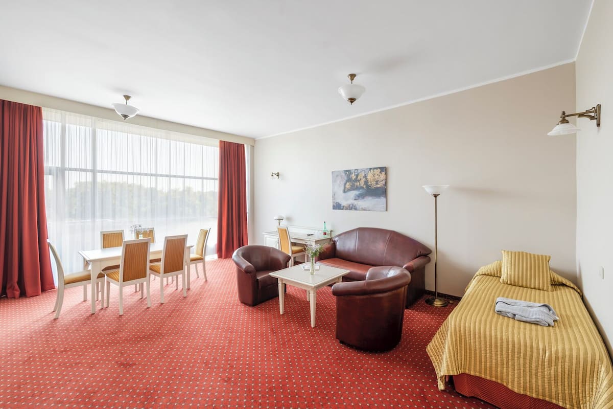 Une chambre d’hôtel comprenant un coin repas, un canapé, un lit et une grande fenêtre avec des rideaux.