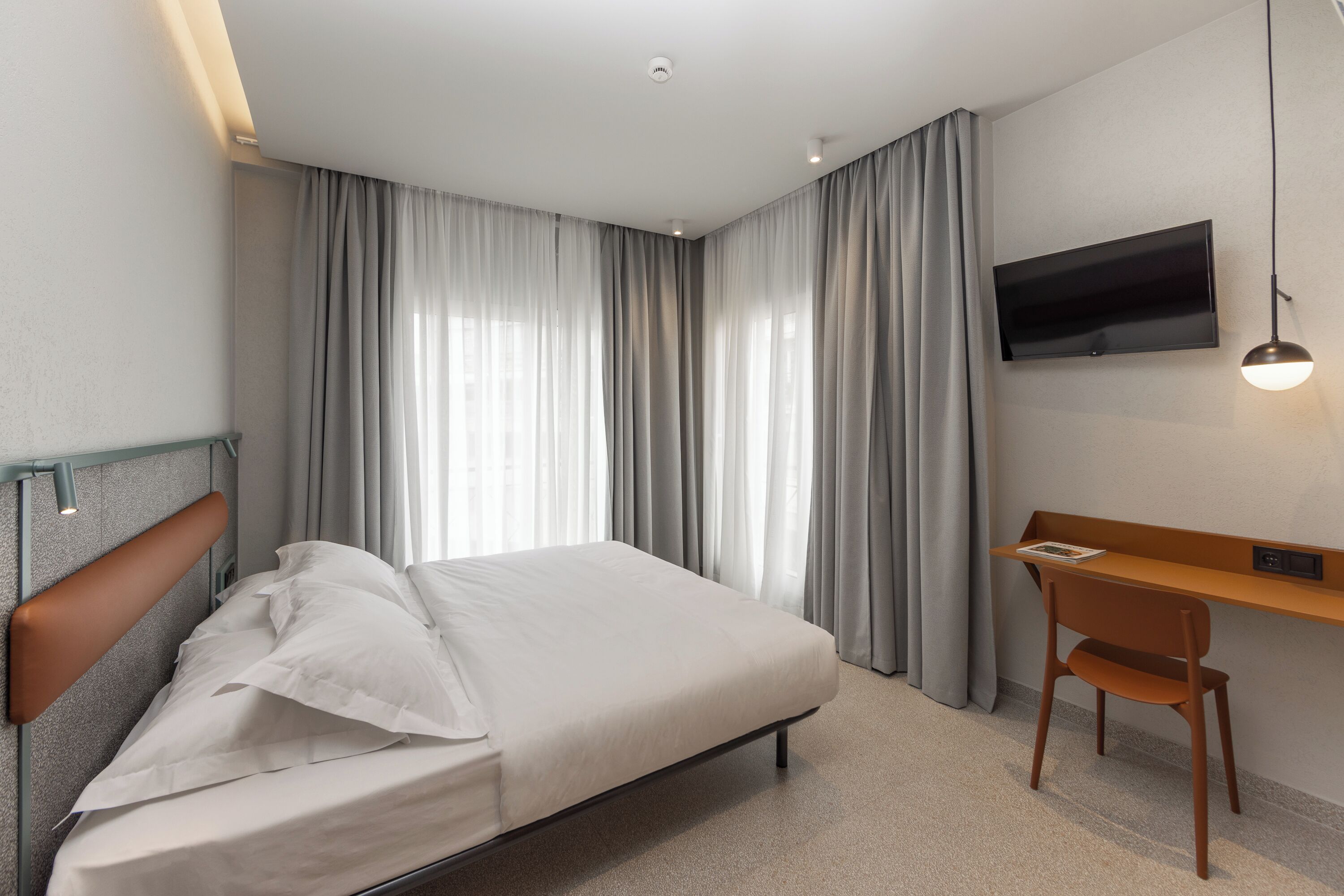 Une chambre d’hôtel équipée d’un lit, d’un bureau et d’un téléviseur fixé au mur.