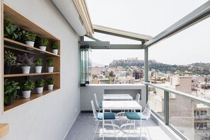 A balcony with a table and chairs, wooden shelves with potted plants, and a view of a cityscape with a hill in the background. - Evripides Hotel (Athens)