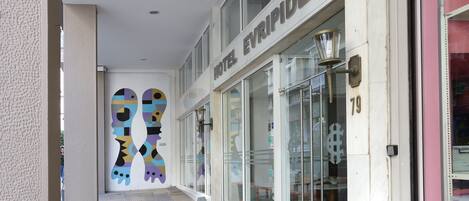 A hotel entrance with a modern design, featuring a glass facade and a colorful mural on the wall.