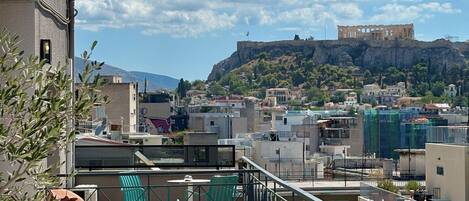 A rooftop terrace with outdoor seating, overlooking a cityscape and a historic building on a hill.