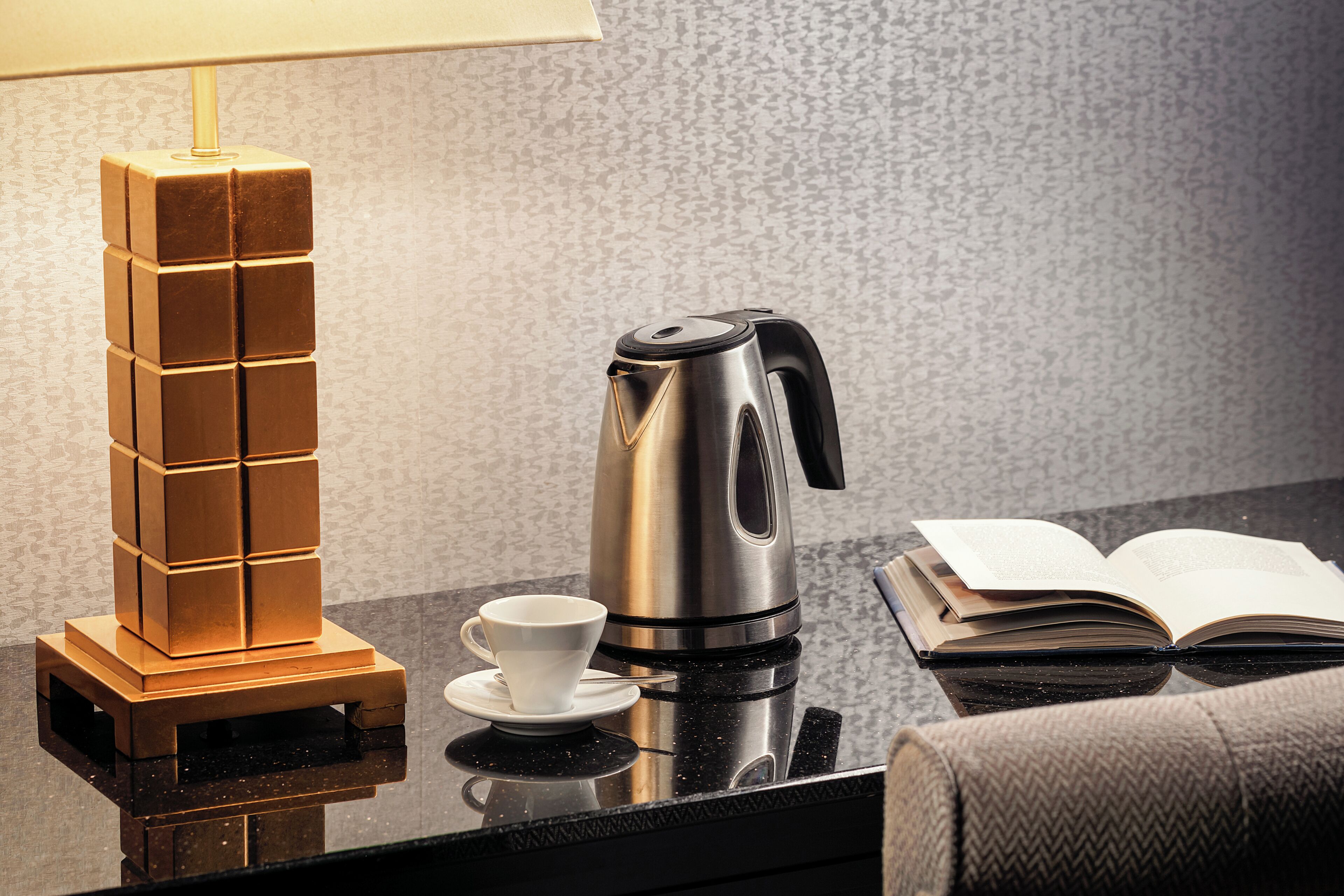 A coffee maker, a stack of cubes, a cup, and an open book on a reflective surface.