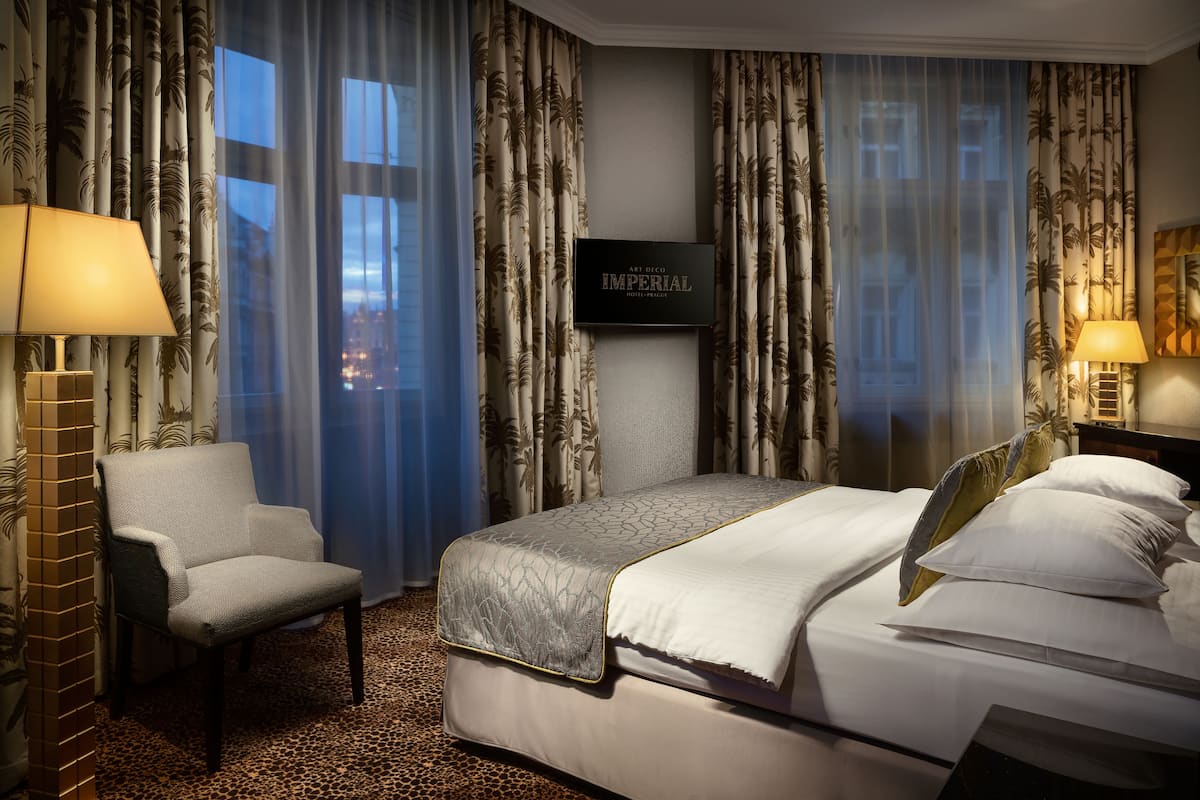 Een hotelkamer met een bed, een stoel, een televisie en gordijnen met een palmbladmotief.