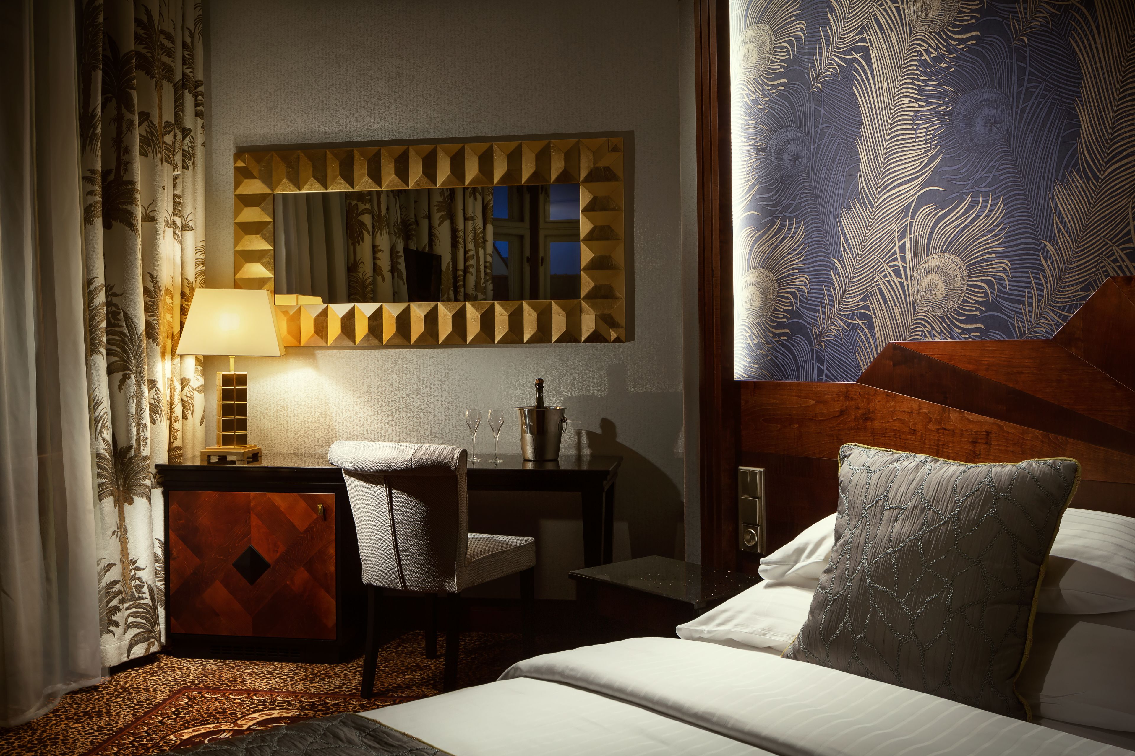 Une chambre d’hôtel comprenant un lit, un bureau avec une lampe, une chaise, une table de chevet et un grand miroir.