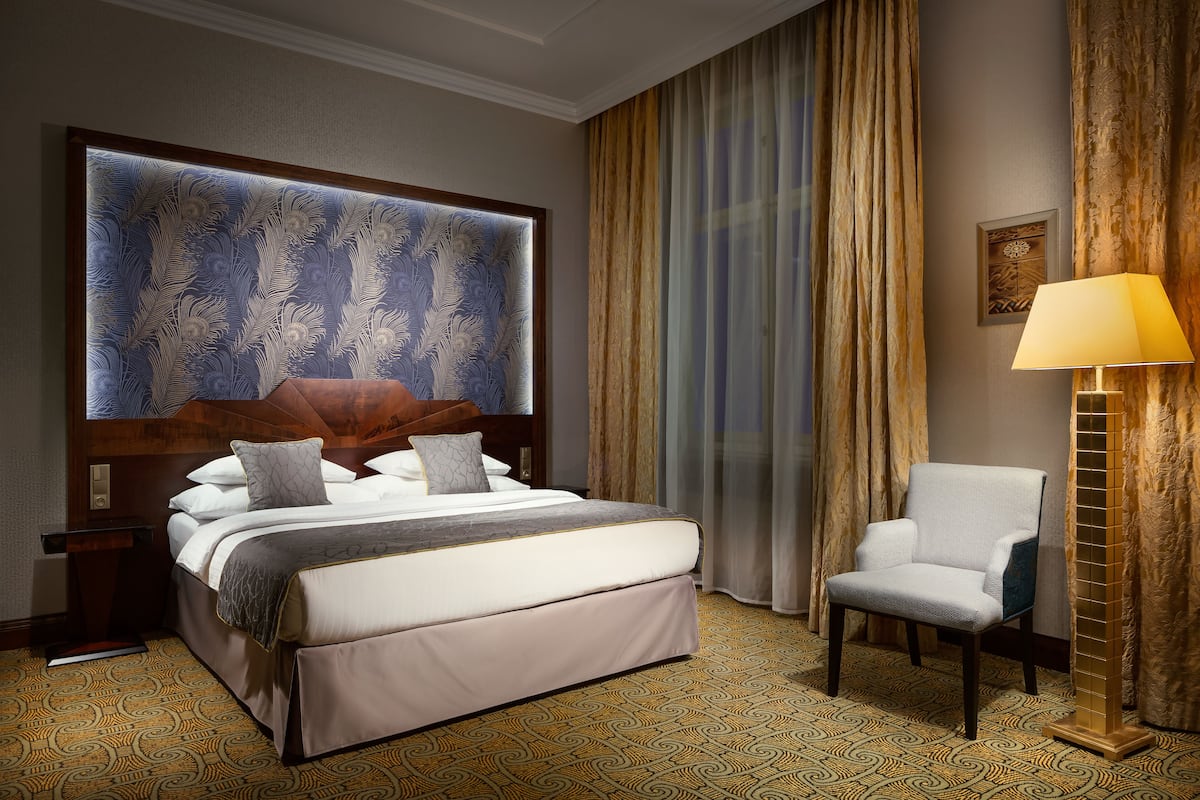 Een hotelkamer met een groot bed, een stoel, een lamp en een kamerbreed tapijt met dessin.