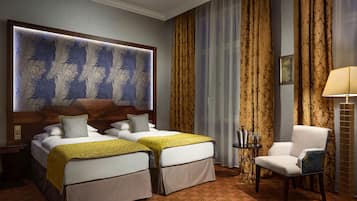 Una camera d'albergo con due letti, una grande testiera decorativa, una sedia, un comodino e una lampada.