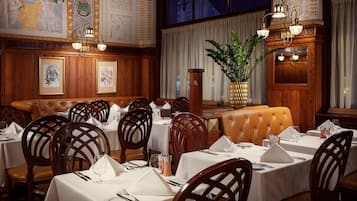 A restaurant with wooden paneling, white tablecloths, and leather booths.