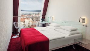 Une chambre d’hôtel avec un grand lit, une table de chevet en verre, une chaise et une vue sur le paysage urbain.