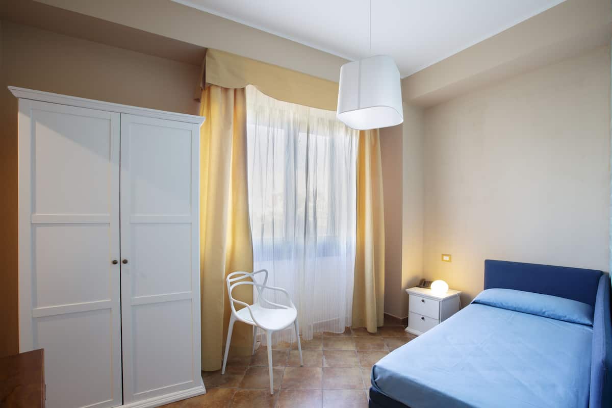 Un dormitorio con cama, armario, silla, mesita de noche y ventana con cortinas.