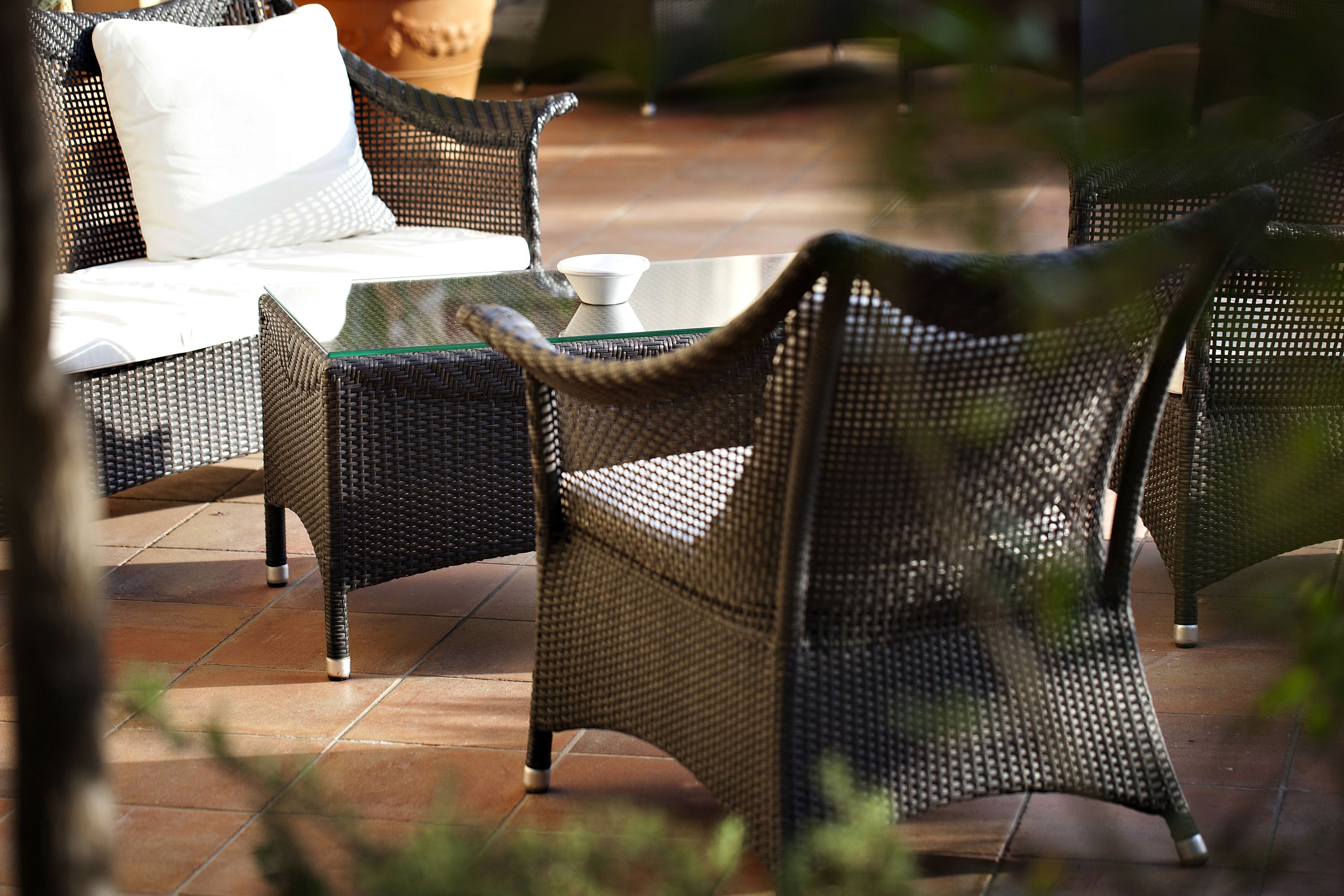 A wicker outdoor seating area with a glass table and white cushions.