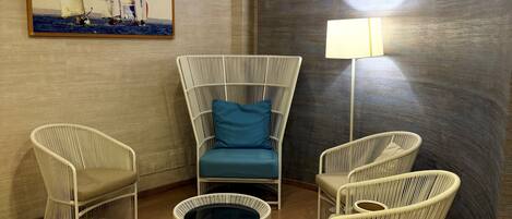 A room with a round table, two chairs, a sofa, a lamp, and a painting of sailboats.