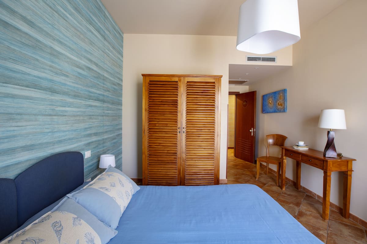 Un dormitorio con una cama, un armario de madera, un escritorio con una silla y un cuadro en la pared.