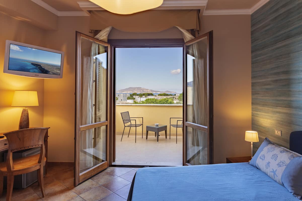 Habitación de hotel con cama, escritorio, silla, mesa y balcón con vista a un paisaje.