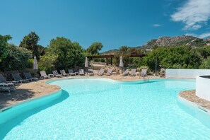 A clear blue swimming pool with lounge chairs and a pergola, surrounded by greenery and mountains. - Hotel Valdiola (Arzachena)