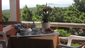 A table set with tea cups, a teapot, and a plant, overlooking a forested landscape. - Hotel Valdiola (Arzachena)