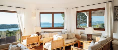 Un amplio salón con mobiliario de mimbre, ventanas grandes y vista a un lago.