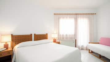 A hotel room with two beds, a bedside table with a lamp, a telephone, and a window with curtains.