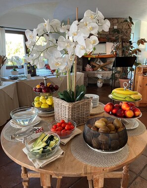 A round wooden table with various food items and a centerpiece of white orchids. - Hotel Valdiola (Arzachena)
