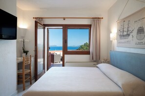 A hotel room with a bed, a desk, a chair, a TV, a window with curtains, and a framed picture on the wall. - Hotel Valdiola (Arzachena)