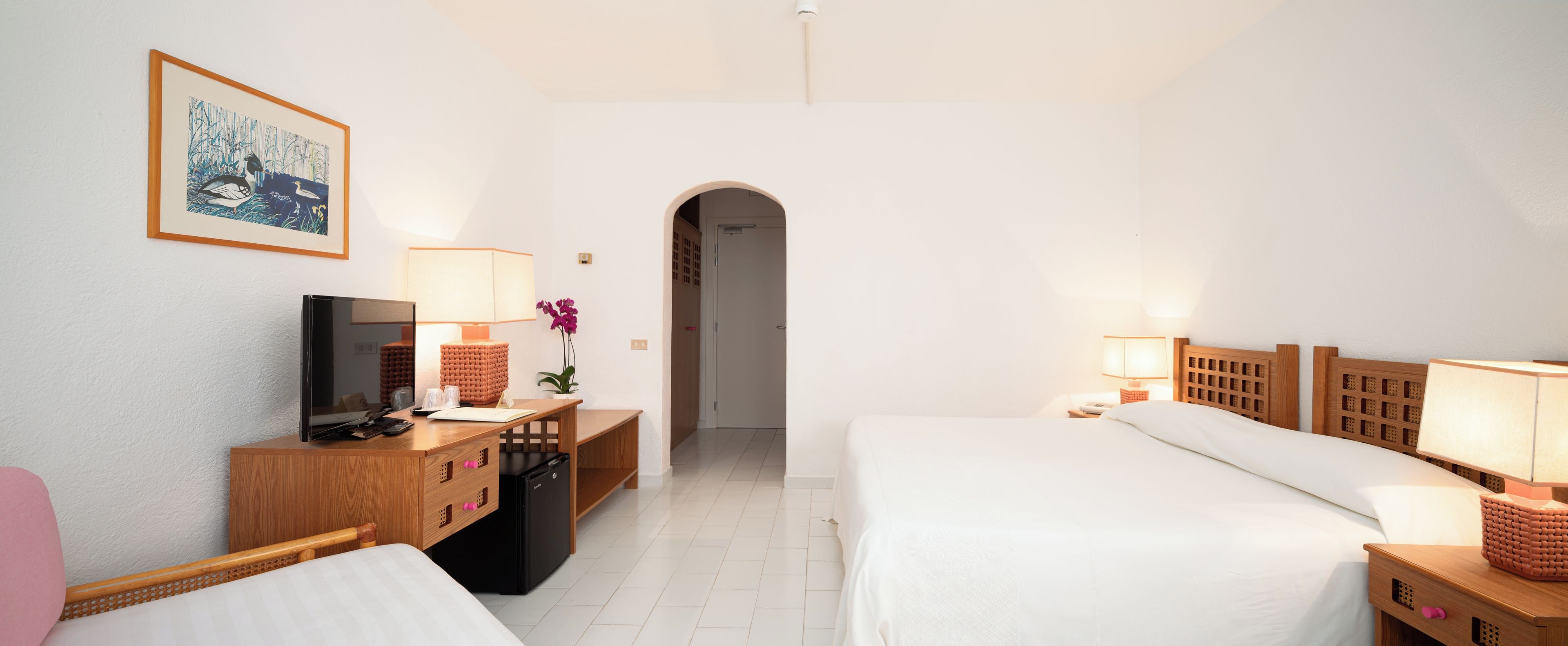 Una habitación de hotel con una cama, un escritorio con computadora, televisión y lámpara.