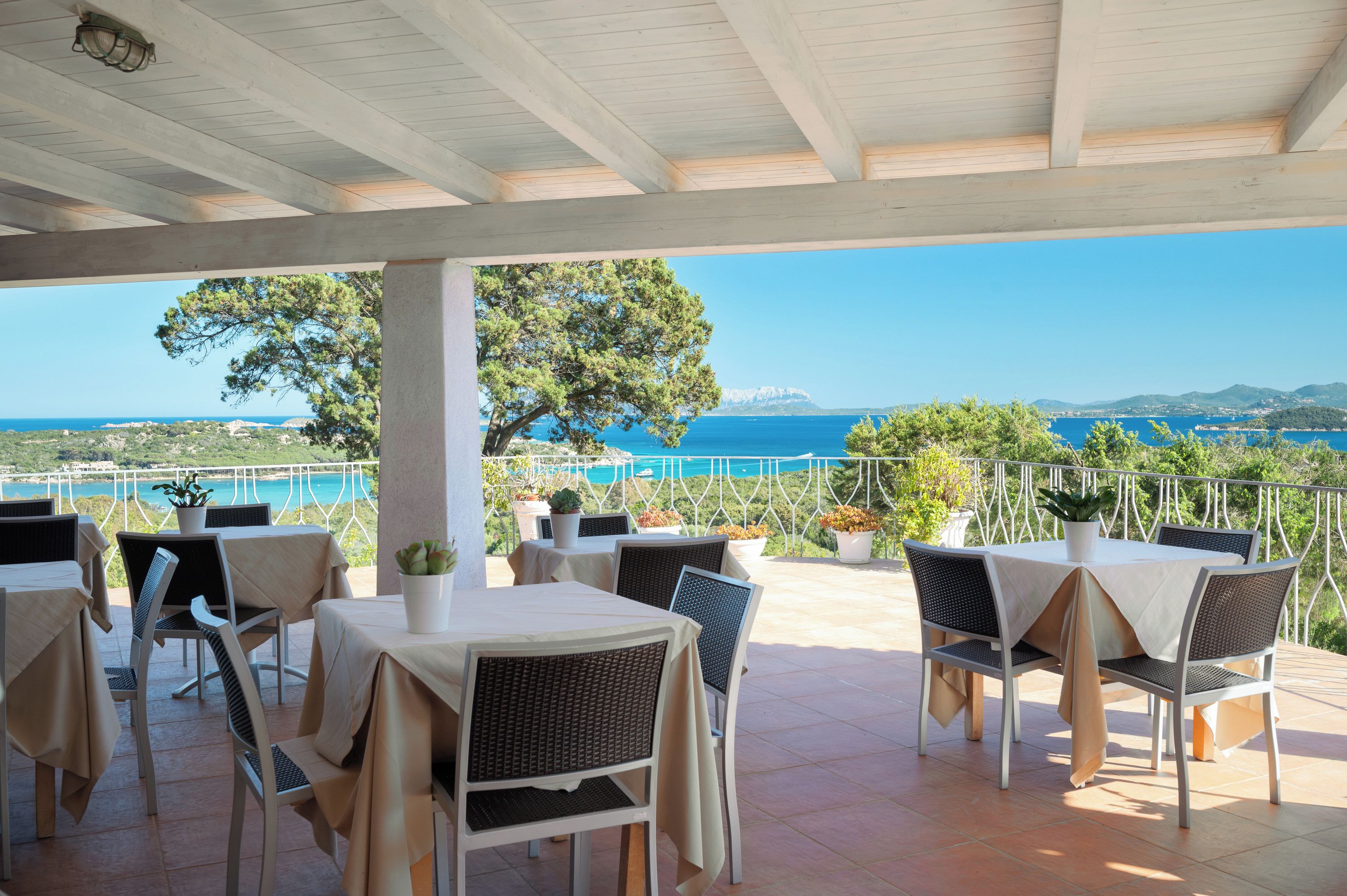 An outdoor terrace with tables and chairs, overlooking a coastal landscape.